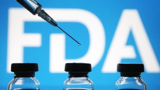 Vials and a medical syringe seen displayed in front of the Food and Drug Administration (FDA) of the United States logo.