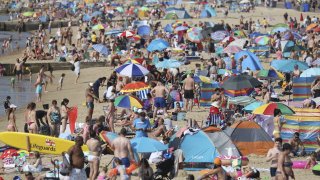 People gather on the beach during hot weather in Bournemouth, southern England, Sunday Aug. 9, 2020. Many Britons are set to bask in another hot day, with clear skies and hot temperatures predicted to continue.