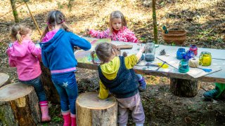 Kindergarten kids having fun drawing and creating on a wooden table in nature.