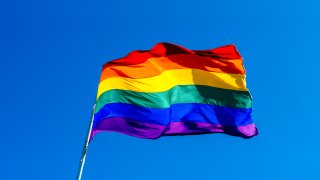Rainbow flag waving in the wind against a clear blue sky