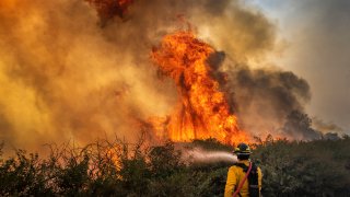 A firefighter braves tall flames as he fights the advancing Silverado Fire fueled by Santa Ana winds at the 241 toll road and Portola Parkway on October 26, 2020 in Irvine, California. (Photo by Allen J. Schaben/Los Angeles Times via Getty Images)