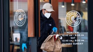 A person wearing a protective mask and gloves exits a Chipotle restaurant in San Francisco, California, April 19, 2021.