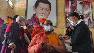 A health worker inoculates a dose of a COVID-19 coronavirus vaccine to a Buddhist monk sitting in front of a portrait of Bhutan's King Jigme Khesar Namgyel Wangchuck (top C) during the first day of vaccination in Bhutan, at Lungtenzampa Middle Secondary school in Thimphu on March 27, 2021.