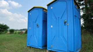 Two portable toilets rest on a field of grass.