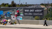 Orange, CA - May 27: Six-year-old Victor Flores, of Orange, walks alone clutching a Pokémon card for comfort, ahead of his family, where his dad said he was sad because he is the same age as 6-year-old shooting victim Adrian Leos, where they prayed and left flowers at a growing makeshift memorial on the Walnut Ave. overpass of the 55 Freeway in Orange May 27, 2021. The memorial featured balloons, toys, cards, messages of love and candles to remember a 6-year-old boy who was shot and killed Friday during an apparent road rage incident on the 55 Freeway. New banners have been placed on the overpass as officials and community continue to increase the reward for arrest of the killer and accomplice. (Allen J. Schaben / Los Angeles Times via Getty Images)