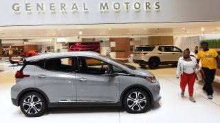 People walk past GM vehicles on display at the General Motors world headquarters building at Detroit’s Renaissance Center.