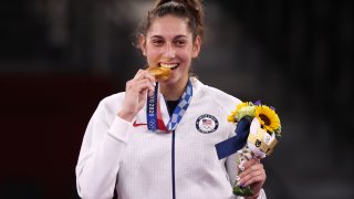 Gold medallist Anastasija Zolotic of the United States bites her medal at a victory ceremony for the women's -57kg taekwondo event during the Tokyo 2020 Summer Olympic Games, at the Makuhari Messe convention center.