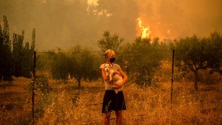 A woman holds a dog in her arms as forest fires approach the village of Pefki on Evia (Euboea) island, Greece’s second largest island, on August 8, 2021.