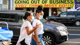 Pedestrians wearing protective masks walk past an out-of-business sign outside a retail store in Harlem, New York City on August 25, 2020.