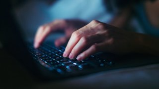 Close-up shot of female hands typing on computer keyboard, lying on bed, working late at home.