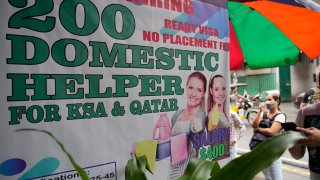 A woman stands beside a sign about hiring domestic helpers for the Mideast outside an office in Manila, Philippines, Oct. 21, 2021.