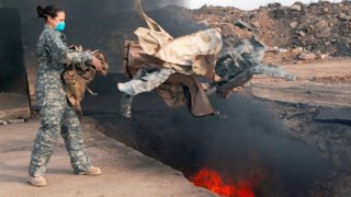U.S. Air Force Senior Airman Frances Gavalis, 332nd Expeditionary Logistics Readiness Squadron equipment manager, tosses unserviceable uniform items into a burn pit at Balad Air Base, Iraq,