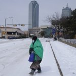 A woman wrapped in a blanket crosses the street near downtown Dallas, Feb. 16, 2021. Much of Texas' power grid collapsed, followed by its water systems, as temperatures plunged and snow and ice whipped the state.