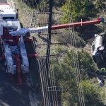 Workers move a car after a rollover accident involving golfer Tiger Woods, Feb. 23, 2021, in Rancho Palos Verdes, California. Woods suffered leg injuries in the one-car accident and was undergoing surgery, authorities and his manager said.