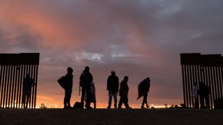 parents-to-be from Haiti stand at a gap in the U.S.-Mexico border wall