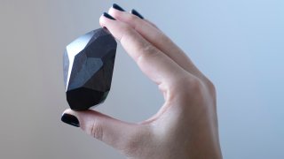 An employee of Sotheby's Dubai presents a 555.55 Carat Black Diamond "The Enigma"