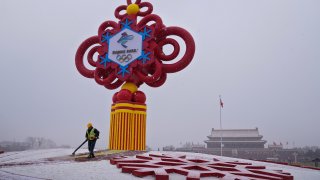 A worker wearing a face mask to protect from the coronavirus uses a blower to clean the snow on a decoration for the Beijing Winter Olympics Games on display at Tiananmen Square in Beijing, Thursday, Jan. 20, 2022. With just over two weeks before the opening of the Beijing Winter Olympics, residents of the Chinese capital say they're disappointed at not being able to attend events because of coronavirus restrictions that have seen parts of the city placed under lockdown.