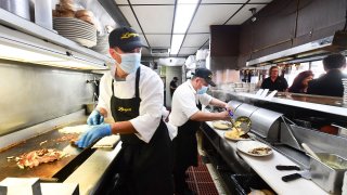 In this photo taken on June 15, 2021 kitchen staff continue wearing face masks while preparing breakfast at Langer’s Delicatessen-Restaurant in Los Angeles, California, on California’s first day of fully reopening its economy after some fifteen months of Coronavirus pandemic restrictions.