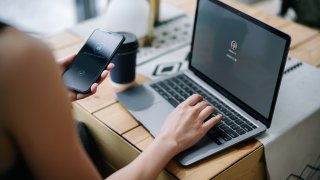 Young businesswoman working on desk, logging in to her laptop and holding smartphone on hand with a security key lock icon on the screen. Privacy protection, internet and mobile security concept