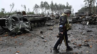 A Ukrainian policeman walks past the wreckage of a Russian armoured vehicle in Dmytrivka village, west of Kyiv, on April 2, 2022 as Ukraine says Russian forces are making a “rapid retreat” from northern areas around Kyiv and the city of Chernigiv.