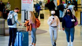 Travelers wearing protective masks as a precaution against the spread of the coronavirus move about the a terminal at the Philadelphia International Airport