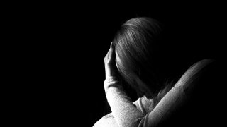 Black and white portrait of a woman hiding her face with hands. Stop violence against woman or mental health concept. Studio shot.