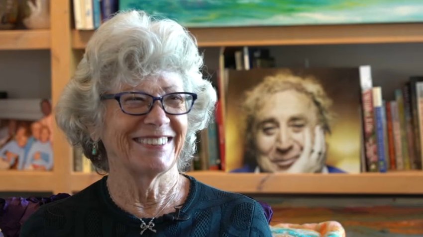 Karen Wilder speaks to NBC 7 on Thursday, April 29, 2022 with a portrait of her late husband, Gene Wilder, in the background.