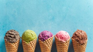 Various ice cream scoops in cones with copy space. Colorful ice cream in cones chocolate, strawberry, blueberry, pistachio or matcha, biscuits chocolate sandwich cookies on blue background.