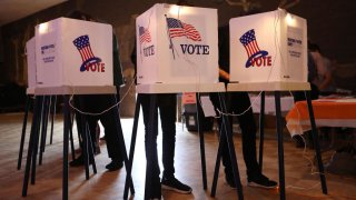 Voters cast ballots behind privacy screen, only their legs are shown