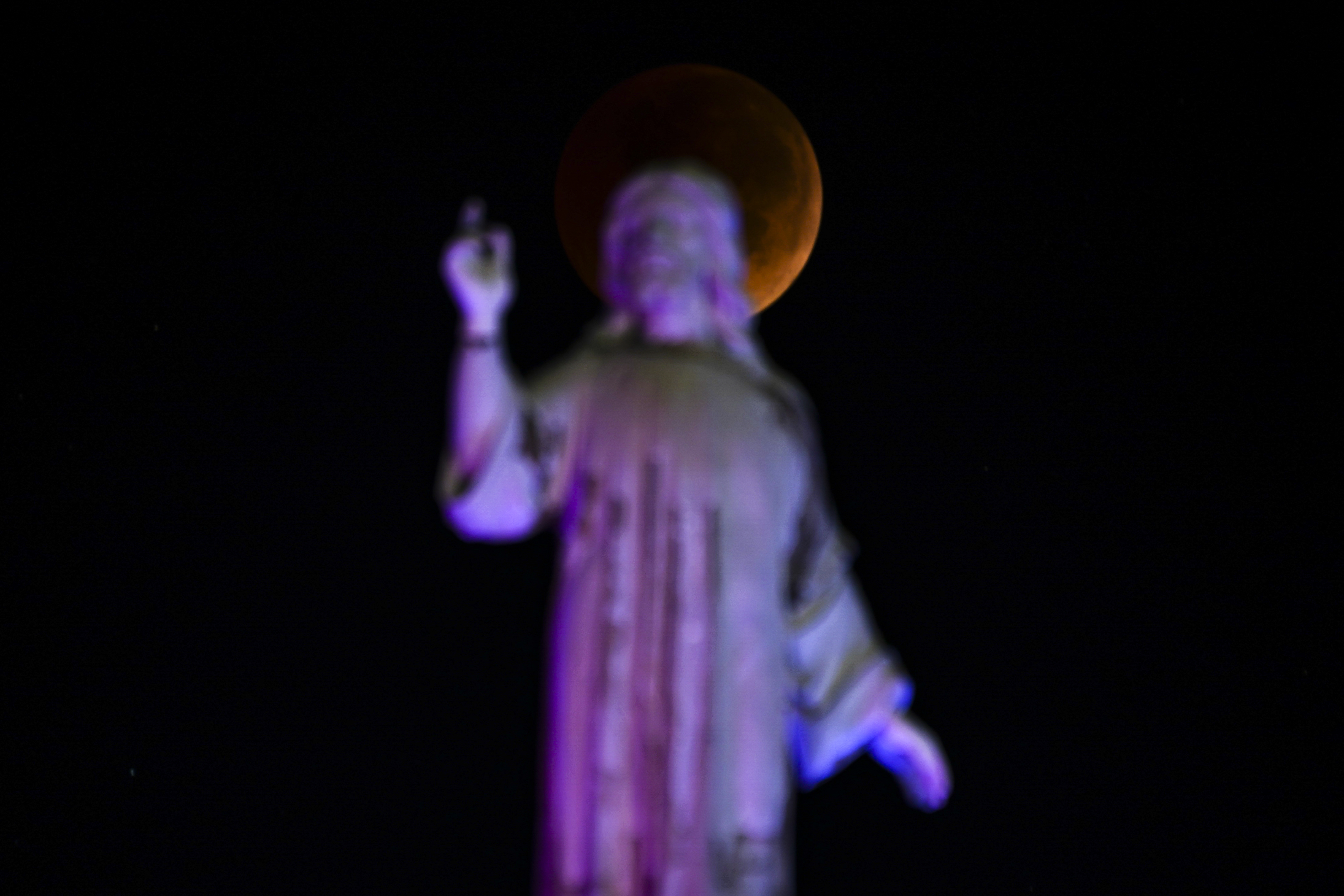 The blood moon sets behind the Salvador del Mundo monument during a total lunar eclipse in San Salvador, El Salvador, Nov. 8, 2022.