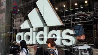 Pedestrians walk by a large Adidas logo inside the German multinational sportswear shop.