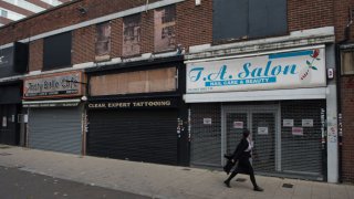 A woman walks past rundown, shuttered shops in Romford, England.