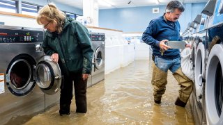 Pamela and Patrick Cerruti empty coins from Pajaro Coin Laundry as floodwaters surround machines in the community of Pajaro in Monterey County, Calif., March 14, 2023. "We lost it all. That's half a million dollars of equipment," said Pamela who added that they plan to rebuild.