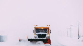 Front side of a sand/plow truck clearing snow on a highway during a blizzard.