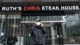 A pedestrian wearing a protective mask walks past a Ruth’s Chris restaurant in Washington, D.C., on Monday, April 20, 2020.