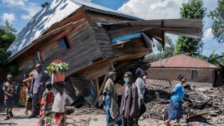 People walk next to a house destroyed by the floods in the village of Nyamukubi, South Kivu province, in Congo, Saturday, May 6, 2023.