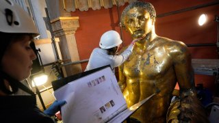 Vatican Museum restorers Chiara Omodei Zorini, left, and Alice Baltera work on the bronze Hercules statue, in the Round Hall of the Vatican Museums, Thursday, May 11, 2023.