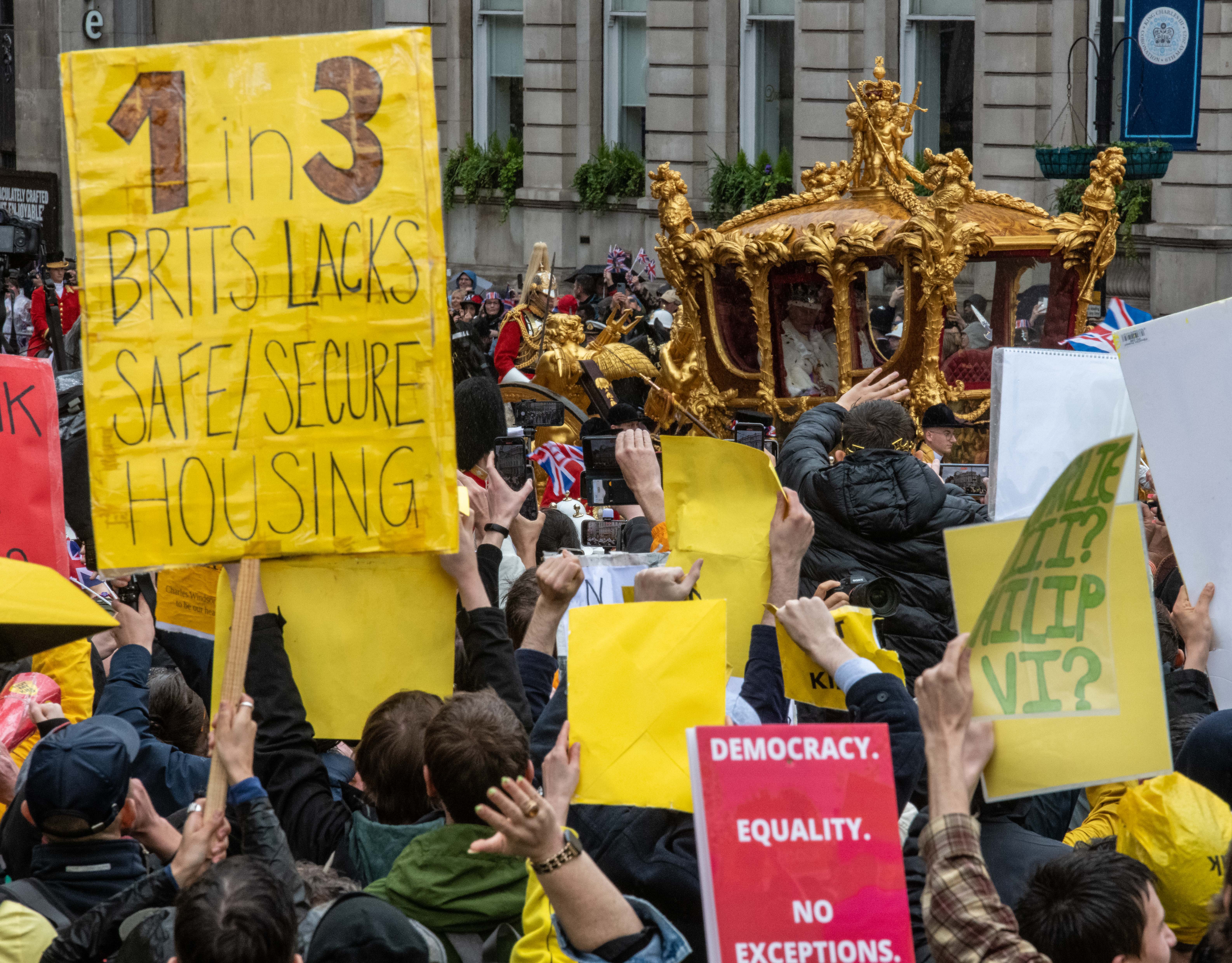 Protesters at Trafalgar Square hold signs and shout as King Charles III and Queen Camilla pass by in the state carriage after the coronation ceremony on May 6, 2023, in London, England.