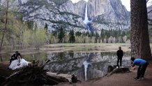 A couple sits for photos as another person stands for a photo in front of Yosemite Falls on April 28, 2023 in Yosemite National Park, California.