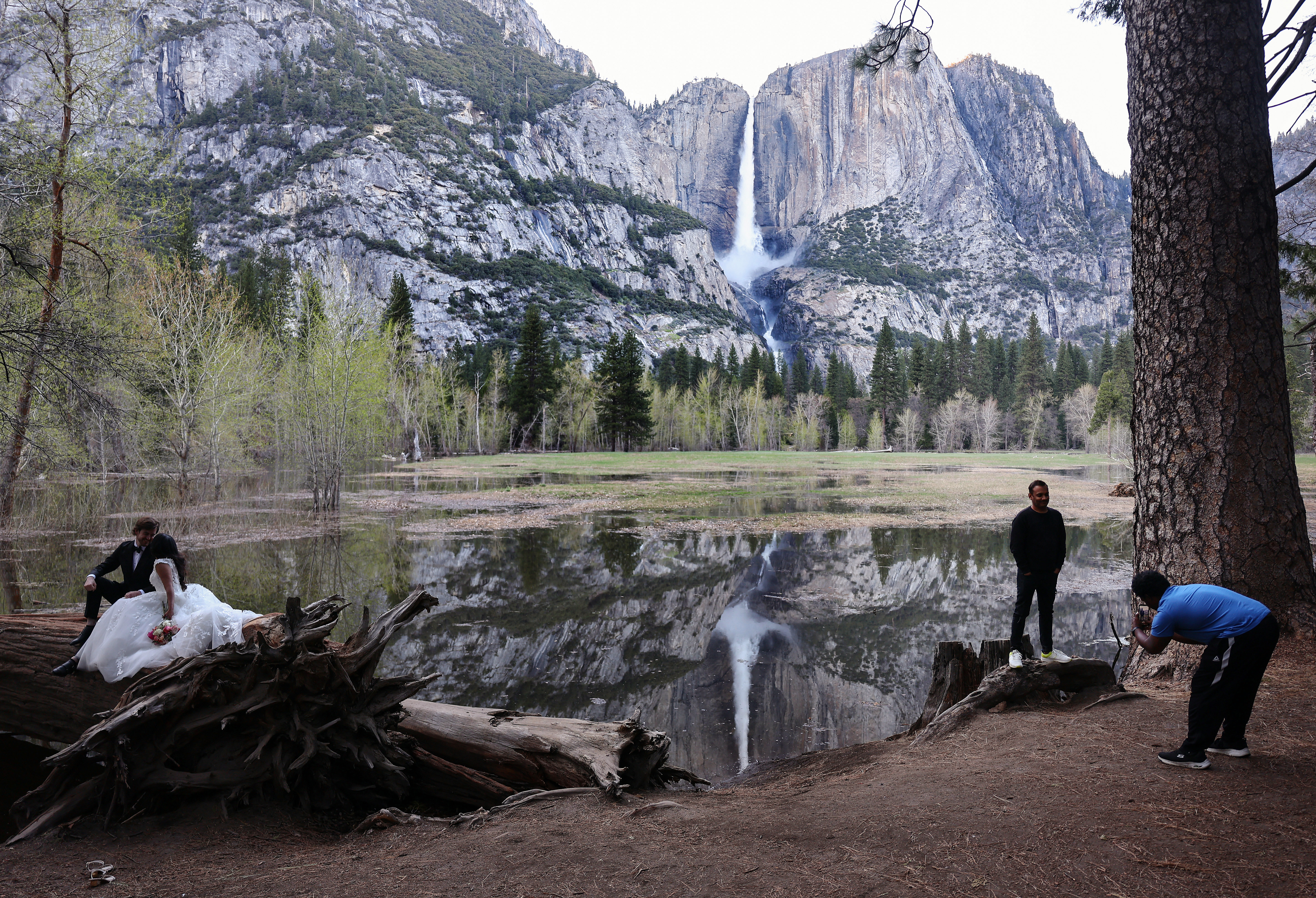 A couple sits for photos as another person stands for a photo in front of Yosemite Falls on April 28, 2023 in Yosemite National Park, California. 