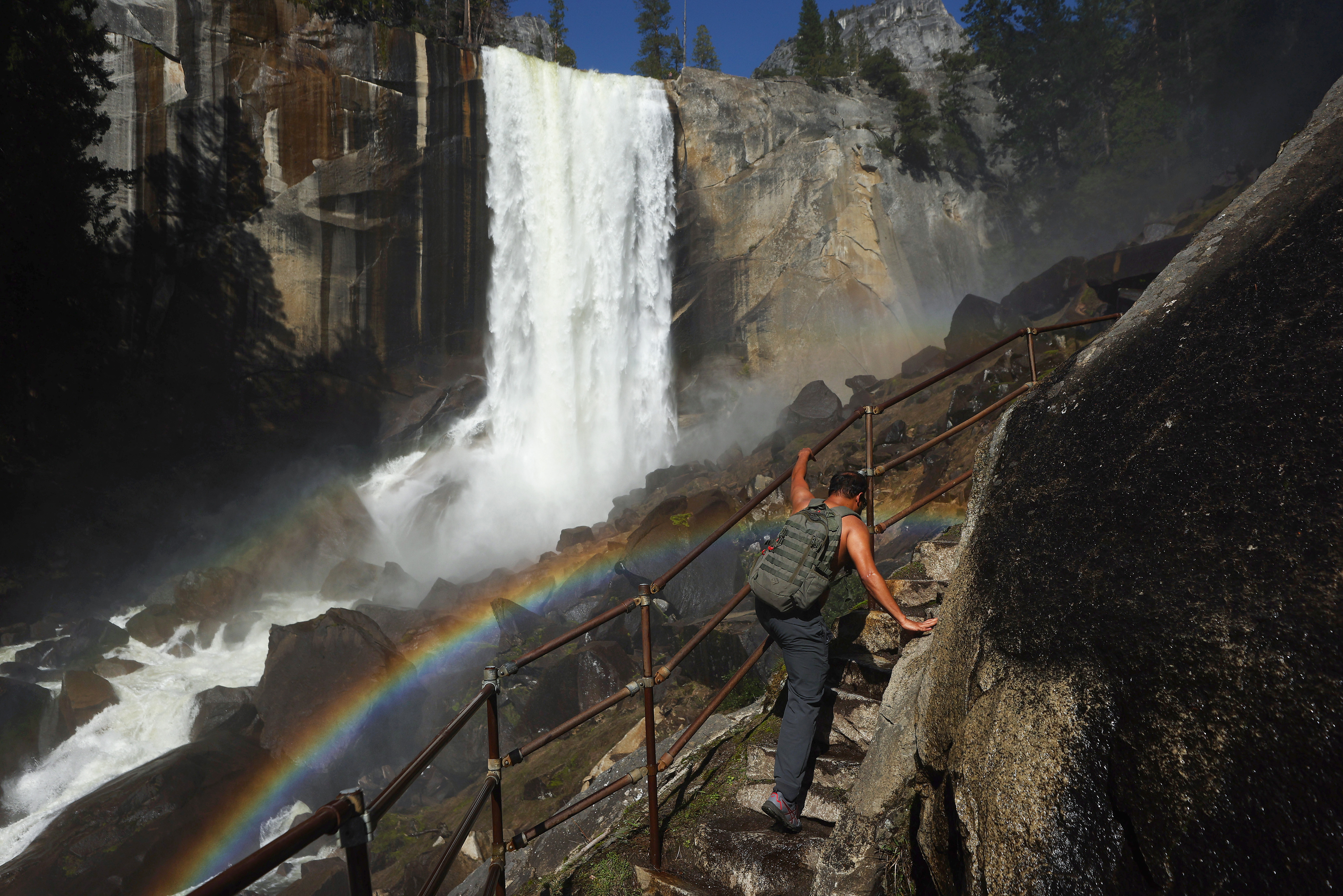A person climbs a stairway leading to the top of Vernal Fall, with a rainbow visible, as warming temperatures have increased snowpack runoff, on April 28, 2023 in Yosemite National Park, California. 