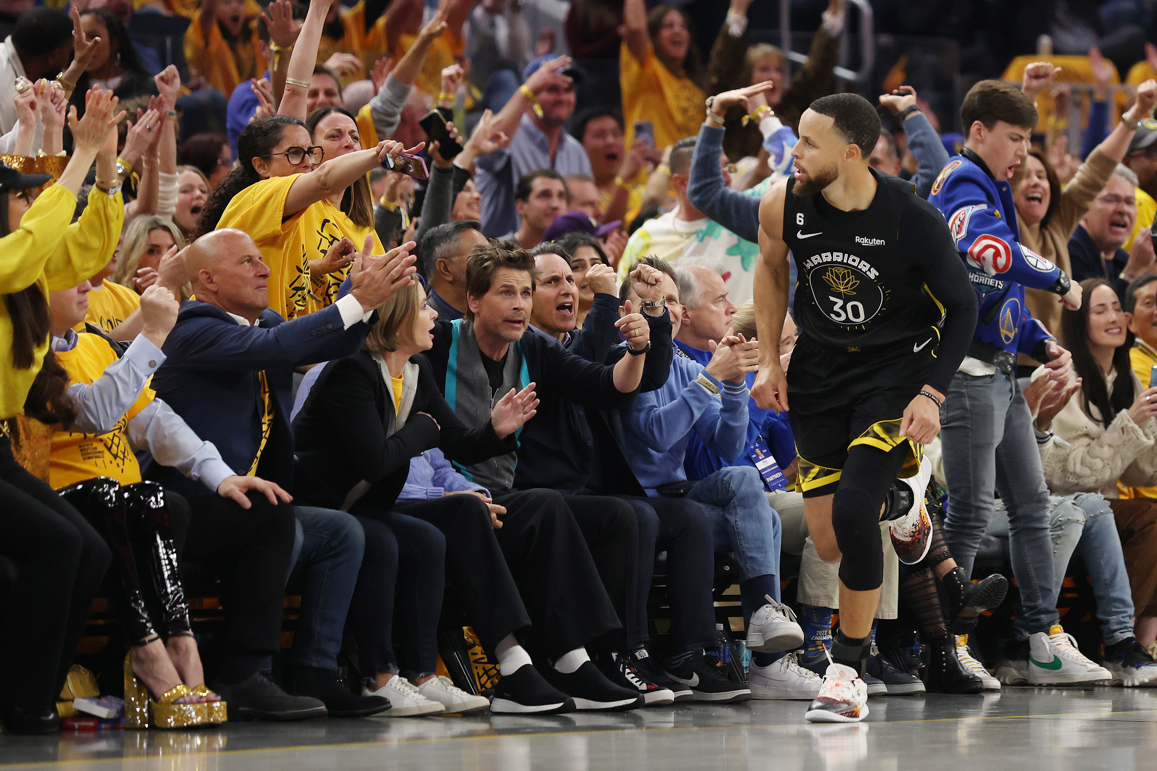 Stephen Curry #30 of the Golden State Warriors celebrates after making a basket as actor Rob Lowe reacts.