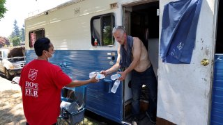 Shanton Alcaraz from the Salvation Army Northwest Division gives bottled water to Eddy Norby who lives in an RV and invites him to their nearby cooling center for food and beverages during a heat wave in Seattle, Washington, U.S., June 27, 2021.