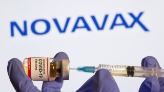 A woman holds a small bottle labeled with a “Coronavirus COVID-19 Vaccine” sticker and a medical syringe in front of a Novavax logo in this illustration taken Oct. 30, 2020.