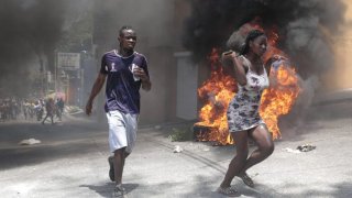 Demonstrators run past tires set on fire during a protest against insecurity in Port-au-Prince, Haiti, Monday, Aug. 7, 2023. (AP Photo/Odelyn Joseph)