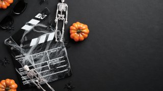 Halloween scary movie concept. Flat lay composition with clapper board, skeleton, spider web, pumpkins on black desk. Halloween background.
