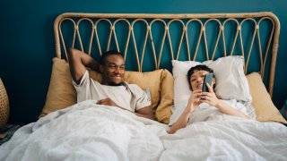 FILE – Smiling girlfriend sharing smart phone with boyfriend while lying on bed