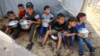 Palestinian children receive food between tents set up for Palestinians seeking refuge on the grounds of a United Nations Relief and Works Agency for Palestine Refugees (UNRWA) centre in Khan Yunis in the southern Gaza Strip on October 24, 2023, amid the ongoing battles between Israel and the Palestinian group Hamas.