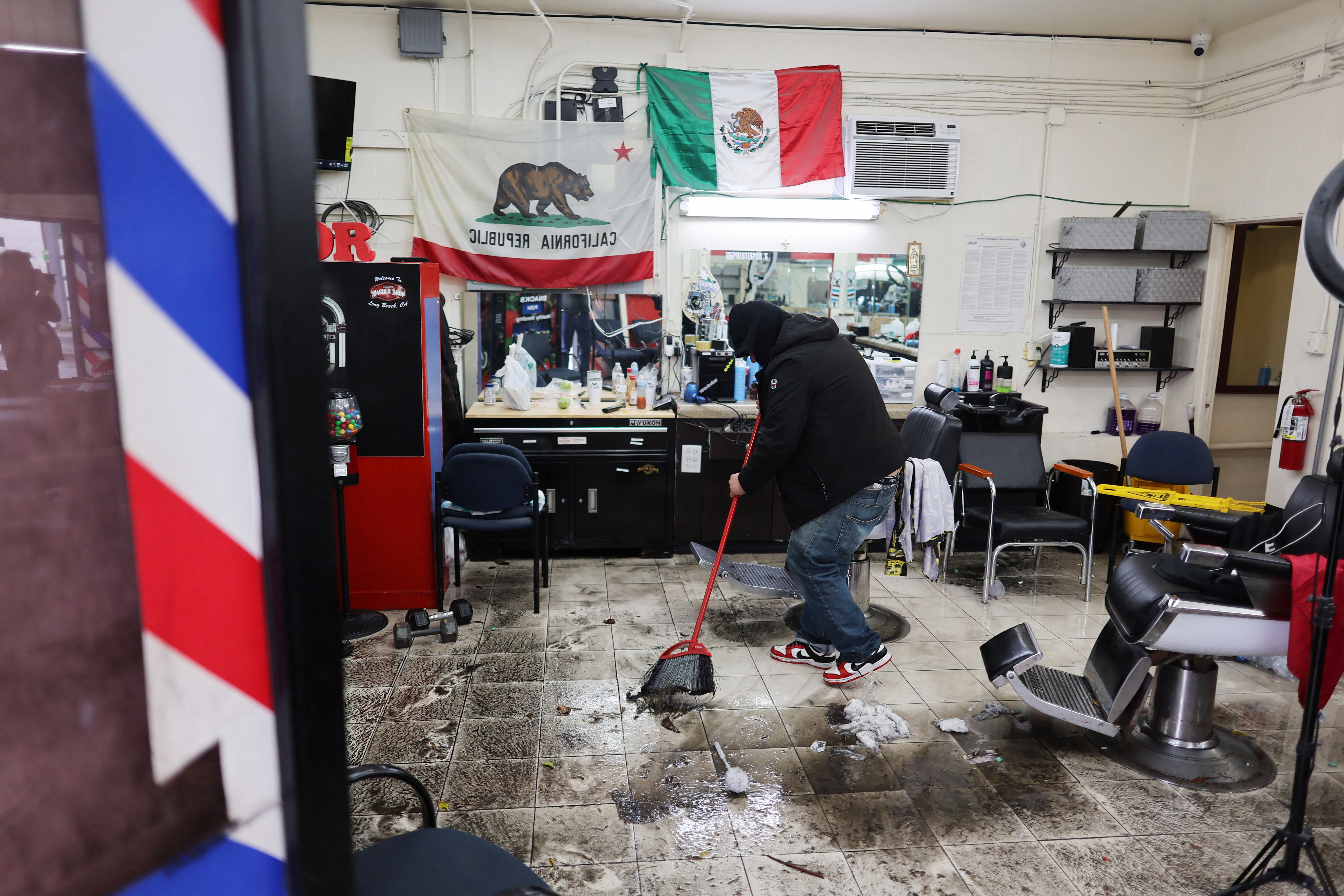 A man sweeps floodwater inside his barbershop during a rain storm in Long Beach, California, on February 1, 2024. The US West Coast was getting drenched February 1, 2024 as the first of two powerful storms moved in, part of a “Pineapple Express” weather pattern that was washing out roads and sparking flood warnings. (Photo by David SWANSON / AFP) (Photo by DAVID SWANSON/AFP via Getty Images)