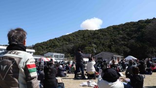 Visitors look on as smoke rises from behind a hill after a small rocket by Tokyo-based startup Space One exploded upon take-off, at the Spaceport Kii site in Kushimoto, Wakayama prefecture on March 13, 2024.